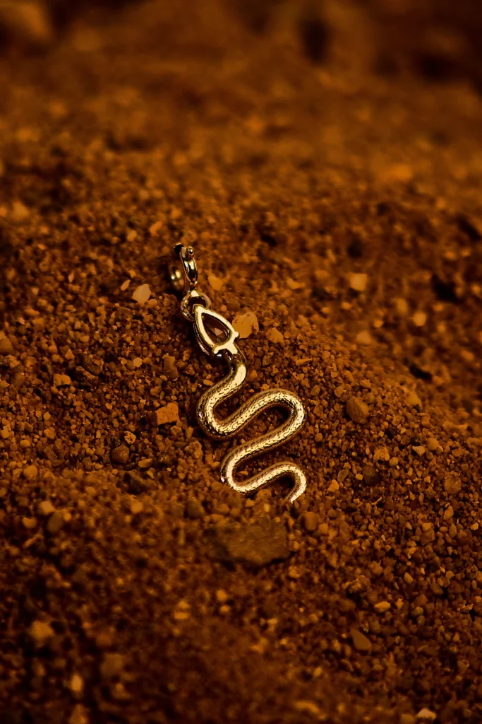 Charm Desiderio Siklah a serpente in oro giallo con pietra a goccia, su sabbia