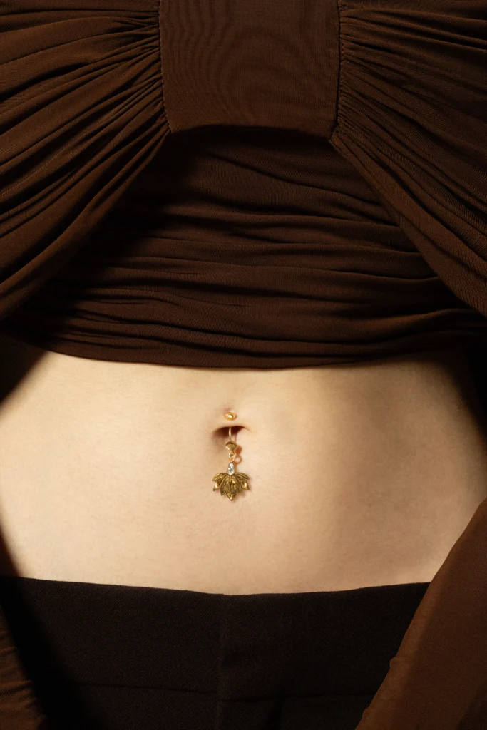 Piercing base Siklah in oro giallo con charm a fiore, indossato con top marrone drappeggiato
