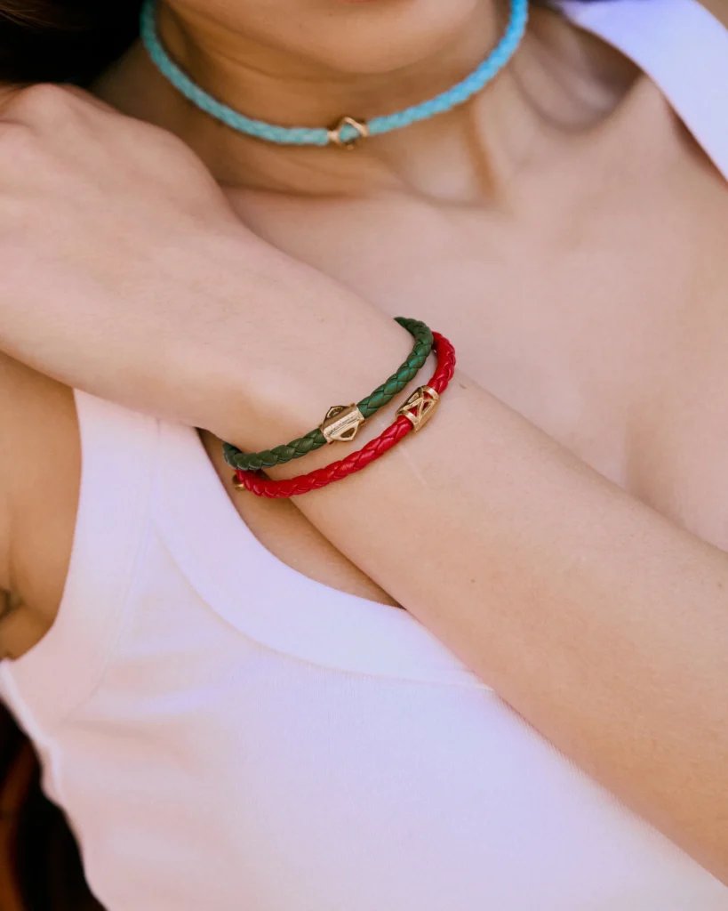 Primo piano al polso dei bracciali Siklah in pelle intrecciata verde e rossa con chiusura dorata