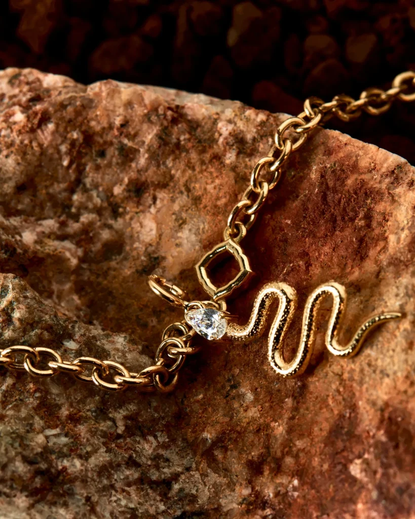 Dettaglio della catena in oro Desiderio Siklah con charm serpente e pietra a goccia, su roccia scura