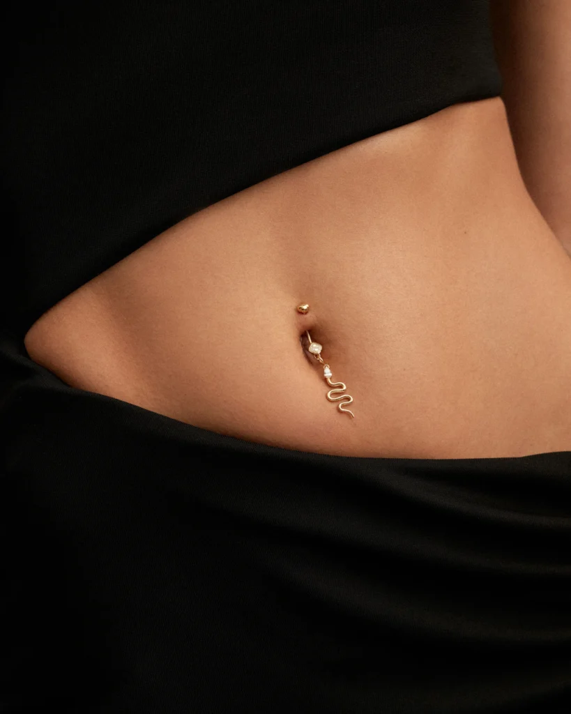 Dettaglio ravvicinato del piercing ombelicale Desiderio Siklah con charm serpente in oro, abito nero