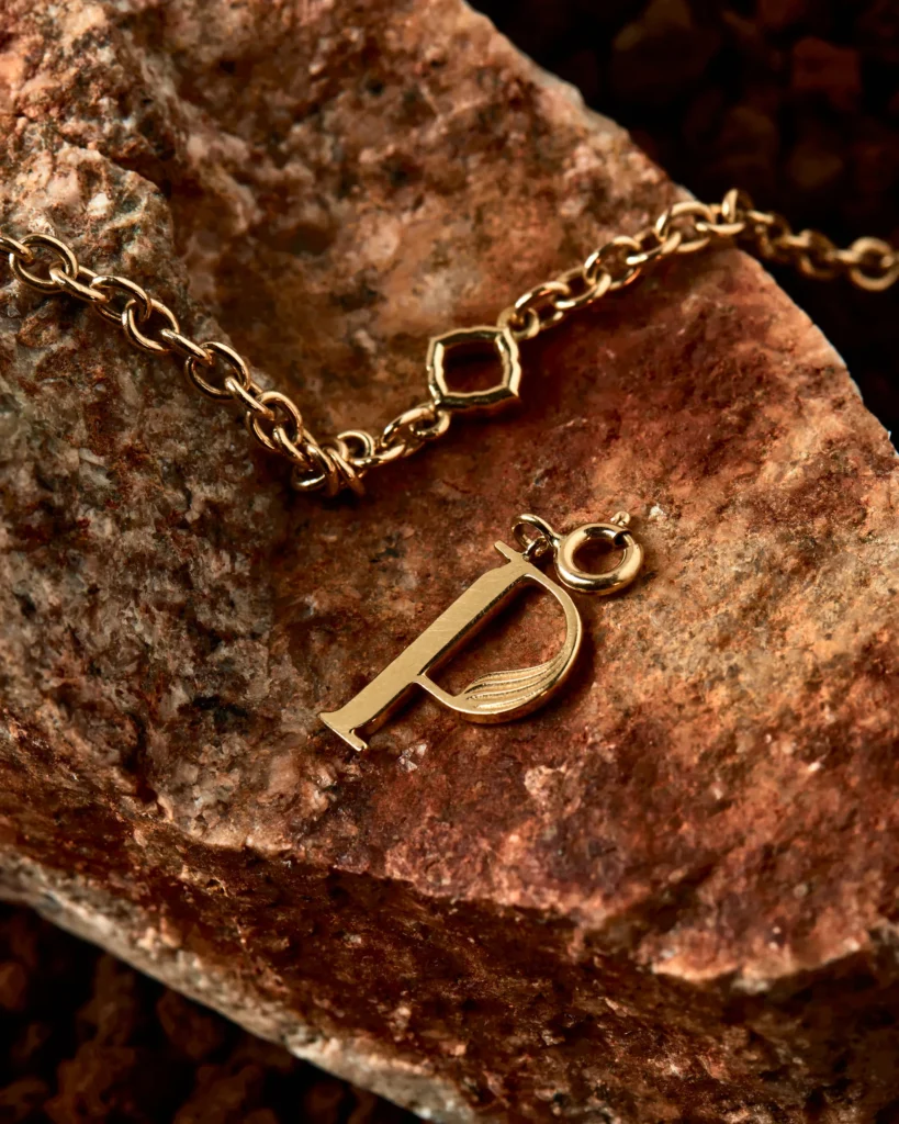Charm Genesi a forma di P in oro giallo Siklah, dettaglio della chiusura su roccia rossastra