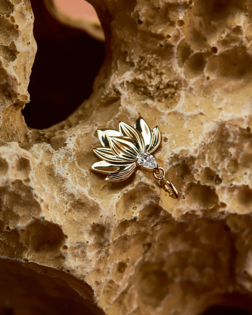 Charm Siklah Incanto in oro 18 carati a forma di loto, in primo piano su roccia beige.