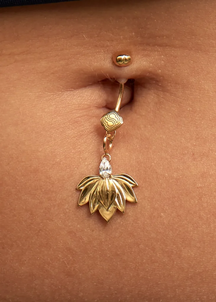Primo piano del charm Incanto Siklah in oro 18 carati agganciato al piercing dell'ombelico.