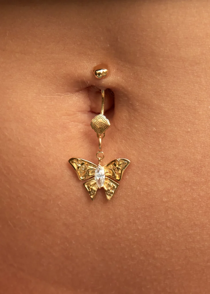 Dettaglio macro del piercing ombelico con charm Sogno Siklah, farfalla in oro e zircone